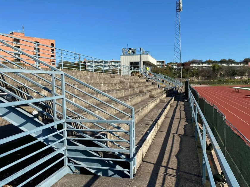 Bleachers next to a running track, with metal railings and control box.