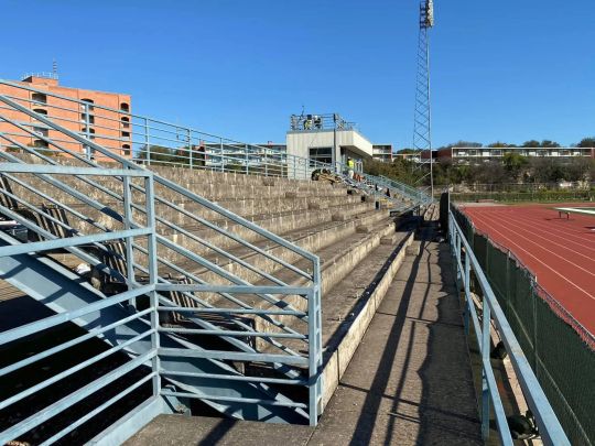 Bleachers next to a running track, with metal railings and control box.
