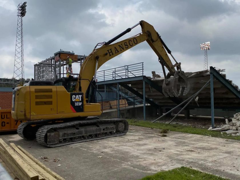 Yellow excavator demolishing a stadium seating area.