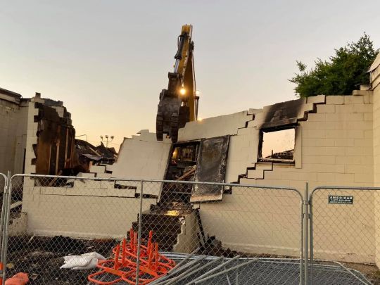 Demolition of a building. An excavator tears down walls under a sunset sky.