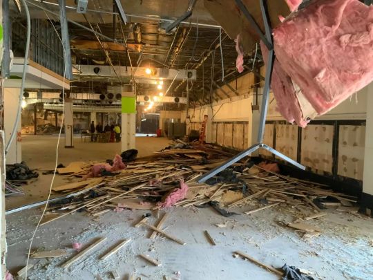 Interior demolition scene, debris covering the floor. Damaged walls and ceiling; exposed insulation.