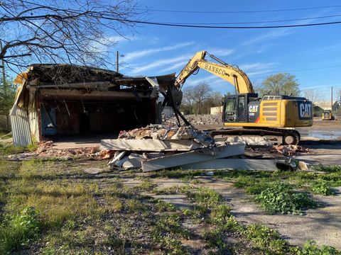 A yellow CAT excavator demolishing a building with a blue sky in the background.