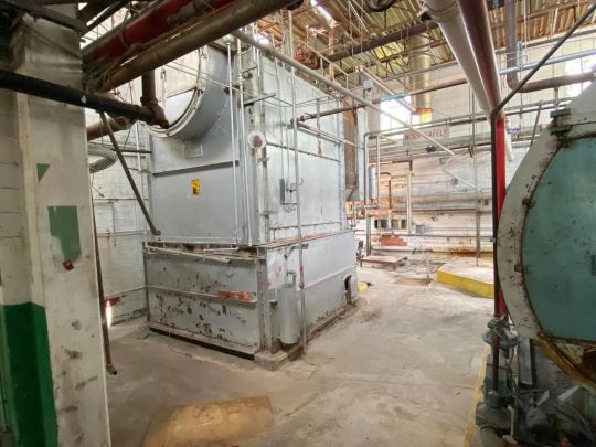 Industrial equipment in a large, empty factory. Gray metal machinery and pipes in a dilapidated setting.