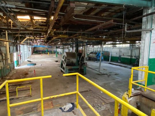 Interior of an industrial building. Empty space with exposed pipes and metal beams, concrete floor, and yellow safety rails.