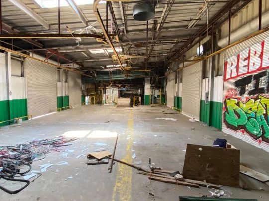 Abandoned industrial interior, graffiti-covered walls, exposed pipes, debris on floor.