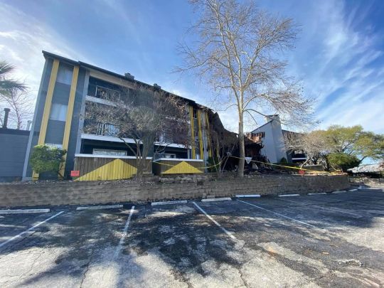 Damaged two-story building with broken windows, debris, and yellow caution barriers outside