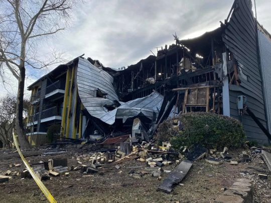 Apartment building heavily damaged by fire; charred structure, debris, cloudy sky.