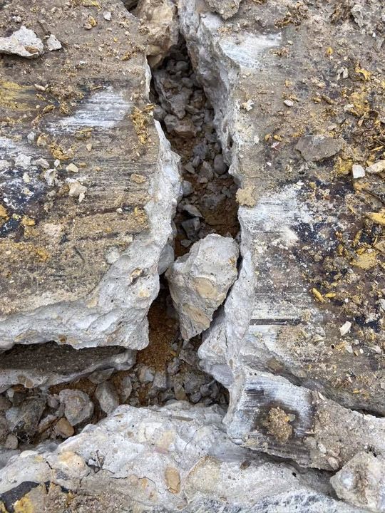 Close-up view of cracked concrete with dirt and small rocks in the crevice.