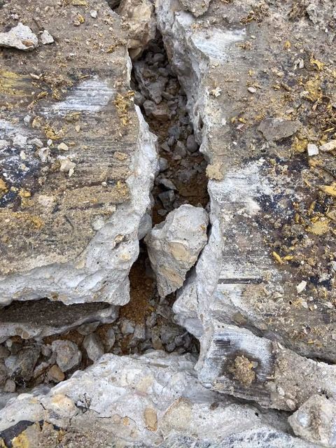 Close-up view of cracked concrete with dirt and small rocks in the crevice.