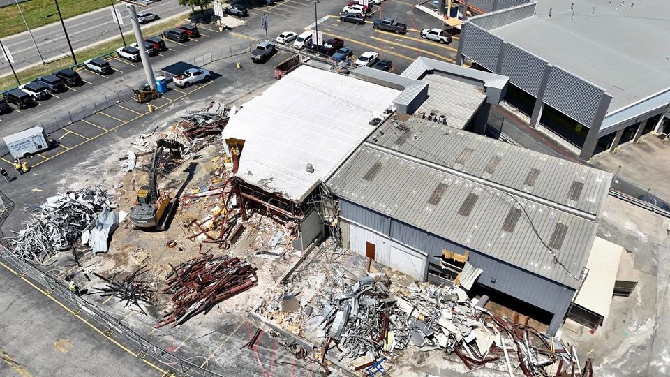 Aerial view of a partly demolished commercial building with scrap metal piles beside a parking lot